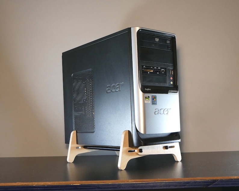May include: A black and silver Acer desktop computer on a light wood stand. The computer has a DVD drive and various ports. The stand is made of light-colored wood and has a simple, functional design. The Acer logo is visible.