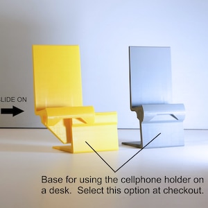 K&ouml;nnte beinhalten: Zwei minimalistische Handyhalter, einer gelb und einer grau, werden gezeigt. Der gelbe Halter befindet sich links und der graue rechts. Der Text "SLIDE ON" und ein Pfeil befinden sich links. Der Text "Base for using the cellphone holder on a desk. Select this option at checkout." befindet sich unten.