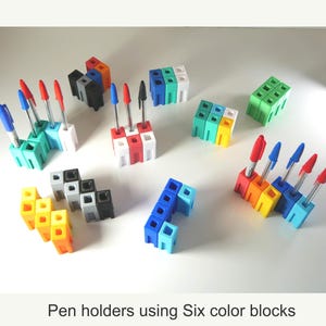 May include: A collection of colorful pen holders made from interlocking blocks. Each holder is a different color, including red, orange, yellow, green, blue, and white. The holders are filled with pens with red and blue ink. The text at the bottom reads: Pen holders using Six color blocks.