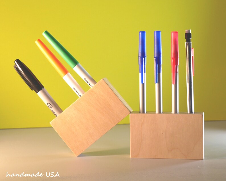 May include: Two wooden pen holders with pens and markers. One holder contains a black Sharpie, orange and green markers. The other holder has blue, red pens and a mechanical pencil. The text "handmade USA" is visible.