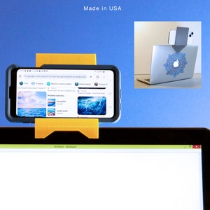K&ouml;nnte beinhalten: Gelber Smartphone-Halter an einem Laptop befestigt, mit einem Smartphone, das eine Google-Suche nach Ozeanbildern anzeigt. Ein zweites Telefon ist am Laptop-Bildschirm befestigt. Der Text "Made in USA" ist sichtbar.