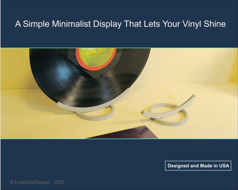 May include: A minimalist vinyl record display stand in light gray. The stand is designed to hold a vinyl record, showcasing its label. The design is simple and modern, with the text "Designed and Made in USA".