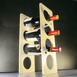 May include: A light-colored wooden wine rack holding three bottles of red wine. The rack has a modern design with circular openings to hold the bottles. The wine bottles have red and gold foil on the top.