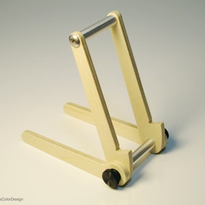 May include: A light-colored wooden stand with a metal bar and black hardware. The stand is designed to hold a tablet or book. The design is simple and functional, with a minimalist aesthetic. The stand is made of wood and metal.