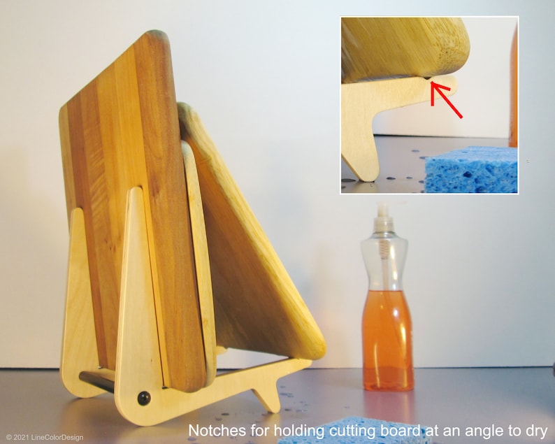 May include: A wooden cutting board stand with a light wood frame and a dark wood cutting board. The stand has notches for holding the cutting board at an angle to dry. The stand is made of light-colored wood and has a black screw.