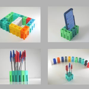 May include: A collection of colorful, 3D-printed desk organizers and accessories. The image shows a phone stand, pen holders, and a modular structure in various colors, including green, blue, yellow, and orange. The items are designed to hold pens, phones, and other small items.