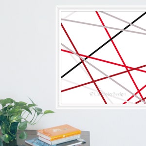 May include: Modern abstract art print. The artwork features a white background with intersecting lines in red, black, and grey. The print is framed in a white square frame. A contemporary piece of wall decor.