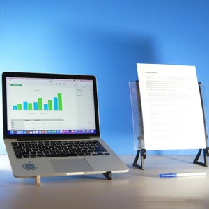 Op de afbeelding: Een zilveren laptop met een staafdiagram, naast een doorzichtige acryl documenthouder met een wit vel papier. Een blauwe pen ligt op het oppervlak. De achtergrond is effen blauw.