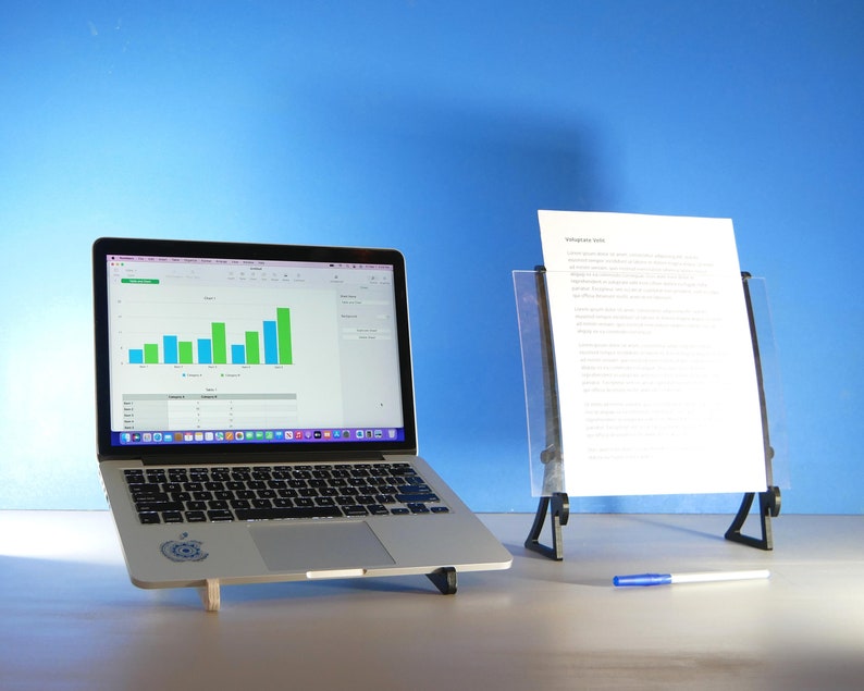 Op de afbeelding: Een zilveren laptop met een staafdiagram, naast een doorzichtige acryl documenthouder met een wit vel papier. Een blauwe pen ligt op het oppervlak. De achtergrond is effen blauw.