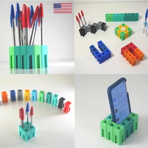 May include: A collection of colorful 3D-printed desk organizers and pen holders. The image showcases various designs, including a phone stand, pen holders, and modular building blocks in shades of green, blue, red, and gray. Pens and a smartphone are displayed.