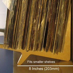 May include: A wooden record shelf, designed to fit smaller shelves. The shelf is light brown and holds a stack of vinyl records. The shelf is 8 inches (203mm) wide.