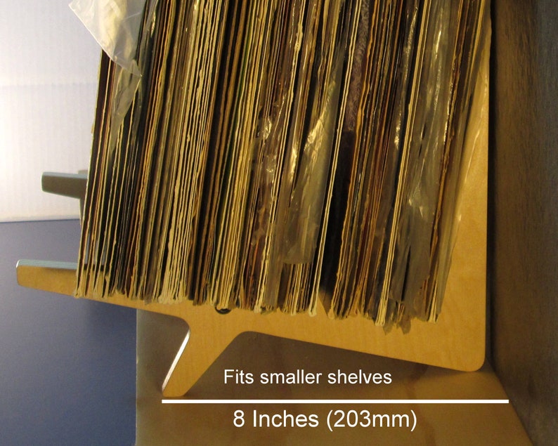 May include: A wooden record shelf, designed to fit smaller shelves. The shelf is light brown and holds a stack of vinyl records. The shelf is 8 inches (203mm) wide.