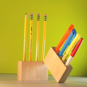 May include: A wooden desk organizer with yellow pencils and colorful markers. The pencils are yellow with pink erasers. The markers are orange, blue, yellow, and red. The organizer is made of light-colored wood.