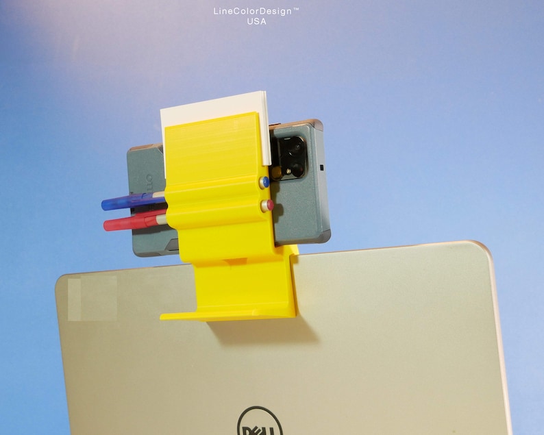 May include: A yellow 3D-printed laptop accessory with a phone holder, pen holders, and a notepad slot. The accessory is attached to a laptop, with a phone and pens in place. The text "LineColorDesign USA" is visible.