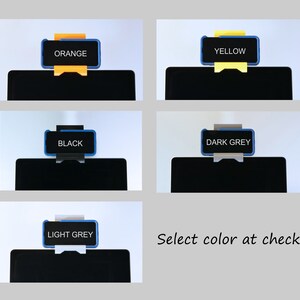 K&ouml;nnte beinhalten: Produktpr&auml;sentation mit f&uuml;nf Farboptionen: Orange, Gelb, Schwarz, Dunkelgrau und Hellgrau. Jede Farbe wird auf einer schwarzen rechteckigen Form angezeigt, mit dem Farbnamen in einem blau umrandeten Rechteck. Der Text "Select color at checkout" ist ebenfalls vorhanden.