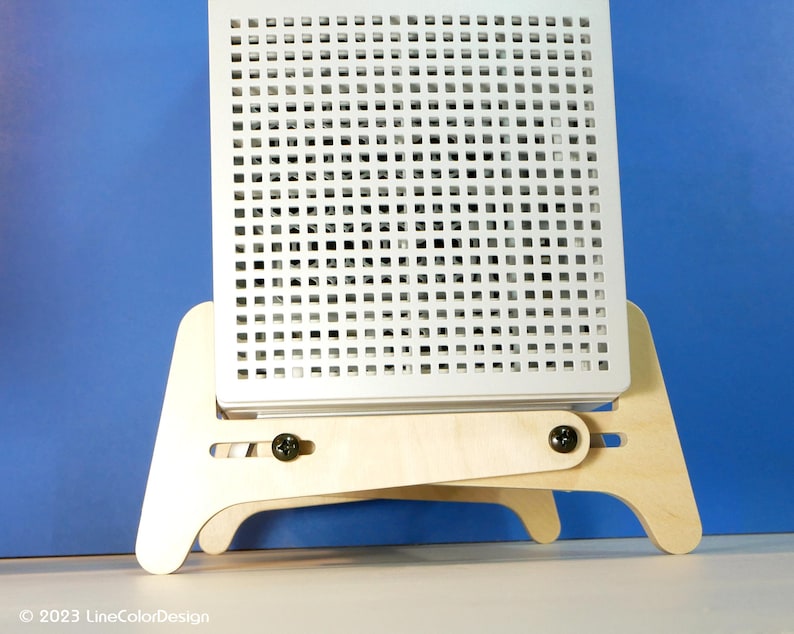 May include: A white, square, perforated panel is mounted on a light wood easel. The easel has a two-piece design with adjustable angles, secured by black screws. The background is a solid blue.