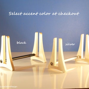 May include: Wooden display stands with a natural finish, featuring a black and silver accent bar. The text "Select accent colour at checkout" is displayed. The stands are on a white surface against a blue background.