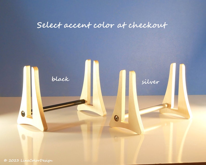 May include: Wooden display stands with a natural finish, featuring a black and silver accent bar. The text "Select accent colour at checkout" is displayed. The stands are on a white surface against a blue background.