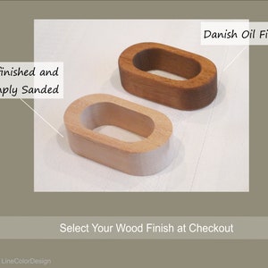 May include: Two wooden oval-shaped objects, one unfinished and sanded, the other with a Danish oil finish. The unfinished piece is light-colored, while the finished piece is a rich brown. Text reads "Unfinished and Simply Sanded" and "Danish Oil Finish".