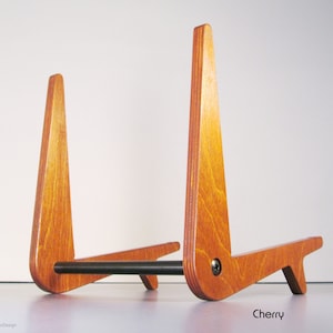 May include: A cherry-stained wooden stand with a black metal bar. The stand has a triangular design with a support base. The word "Cherry" is printed on the bottom right.