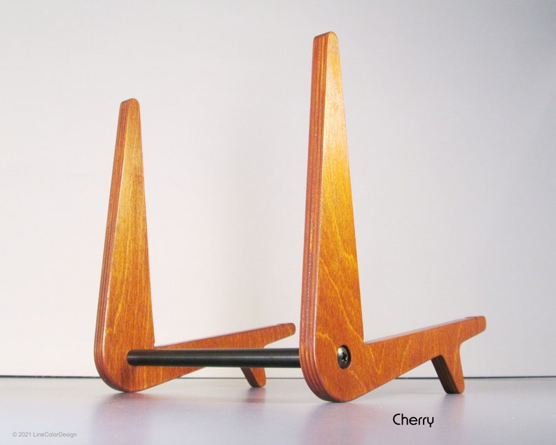 May include: A cherry-stained wooden stand with a black metal bar. The stand has a triangular design with a support base. The word "Cherry" is printed on the bottom right.