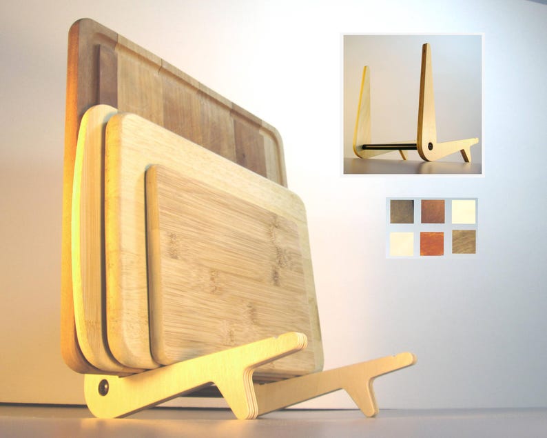 May include: A wooden cutting board set with a light-colored wooden stand. The set includes three rectangular cutting boards of varying sizes, made of light-colored wood. The stand is made of light-colored wood and has a unique, modern design.