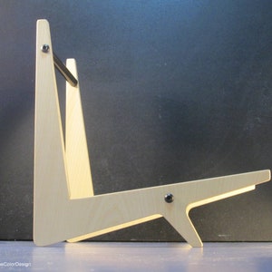 May include: A light-colored wooden guitar stand with a minimalist design. The stand features a triangular frame with a horizontal support and a black metal bar. The stand is held together with black screws. The design is modern and functional.
