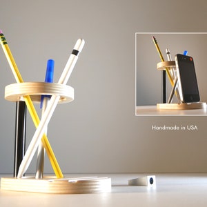 May include: A wooden desk organizer with a circular pen and pencil holder and a rectangular base. The organizer holds pencils, pens, and a smartphone. The text "Handmade in USA" is visible.