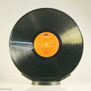 May include: A black vinyl record with an orange and yellow label, displayed on a black stand. The label reads "Sail La Mer" and "Moody Blues". The record is a vintage music item.