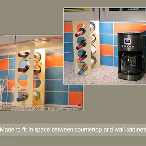 May include: A wooden wine rack with circular openings, holding several bottles of wine. The rack is light-colored and stands on a countertop next to a coffee maker. The background features blue and orange tiled walls. The text says "Made to fit in space between countertop and wall cabinets."