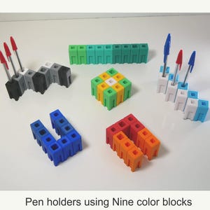 May include: A collection of colorful pen holders made from interlocking blocks. The holders are in various shapes and colors, including black, gray, white, blue, green, yellow, orange, and red. Some holders contain pens with red or blue ink. Text: Pen holders using Nine color blocks.