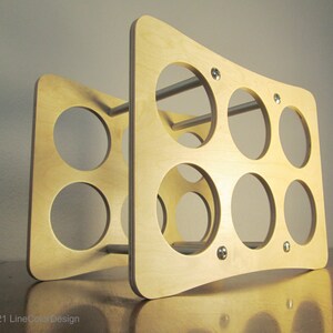 May include: A light-colored wooden wine rack with a curved design. The rack features multiple circular openings for holding bottles and is held together with metal rods and small silver fasteners. The design is modern and minimalist.