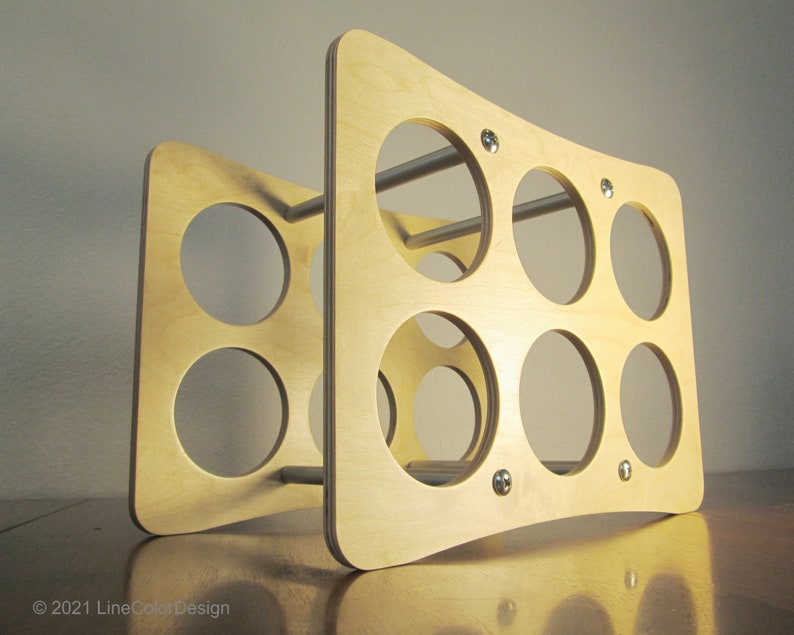 May include: A light-colored wooden wine rack with a curved design. The rack features multiple circular openings for holding bottles and is held together with metal rods and small silver fasteners. The design is modern and minimalist.