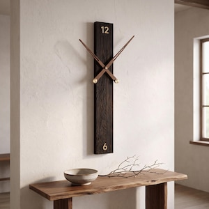 May include: A vertical rectangular wall clock made of dark, textured wood. It features gold-colored numerals 12 at the top and 6 at the bottom. Two long, thin, brown wooden clock hands are positioned in the center with gold-colored accents.
