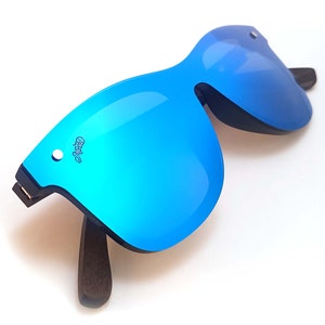 Puede incluir: Gafas de sol azules espejadas con montura de madera oscura. Las gafas tienen una forma angular &uacute;nica.