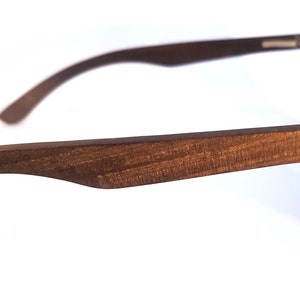 Puede incluir: Vista lateral de unas gafas de sol de madera marr&oacute;n con monturas negras y lentes oscuras. Las gafas de sol tienen la palabra "Marley" grabada en el lateral de la montura.