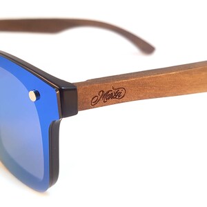 Puede incluir: Gafas de sol azules con espejo y montura de madera. La montura es marr&oacute;n y tiene la palabra "Manzi" grabada.