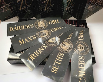 May include: Six black bookmarks with gold lettering and illustrations. The bookmarks feature the names "Darius's", "Max's", "Orion's", "Seth's", and "Caleb's" with a zodiac symbol next to each name.
