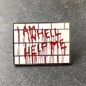 Peut inclure: Une épingle en émail blanc avec un effet de sang rouge qui coule. L'épingle porte l'inscription "I AM HELL HELP ME".