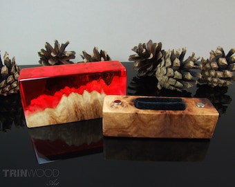 Op de afbeelding: Twee rechthoekige houten dozen. Eén is een rood-oranje hars over een lichtgekleurde houten basis. De andere is een lichtgekleurd hout met een zwart fluwelen inzetstuk en twee zilverkleurige metalen accenten. De dozen worden gepresenteerd met dennenappels.