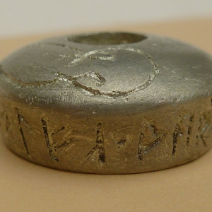 May include: A silver metal ring with a circular design and runes inscribed around the base.