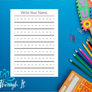 May include: A white handwriting practice sheet with the text "Write Your Name" is displayed on a blue surface. The sheet has solid and dashed lines for writing practice. Colored pencils, a calculator, and other school supplies are also visible.
