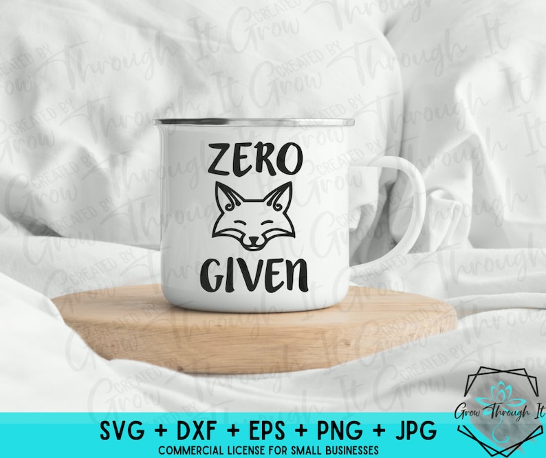 May include: A white ceramic mug with a black outline of a fox and the text "ZERO GIVEN". The mug is sitting on a wooden surface.