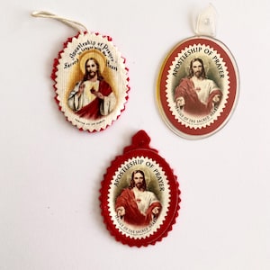 Peut inclure: Trois pendentifs religieux représentant Jésus avec un cœur rouge. Les pendentifs portent l'inscription "Apostolat de la Prière" et "Ligue du Sacré-Cœur". Deux sont ovales, un est rond avec un bord festonné, et tous ont une bordure rouge.