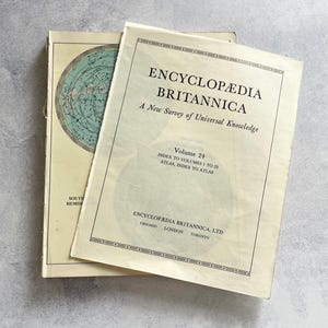 Puede incluir: Dos libros antiguos de tapa blanda con cubiertas de color crema y texto en negro. La cubierta superior dice Encyclopedia Britannica, A New Survey of Universal Knowledge, Volume 24, Index to Volumes 1 to 23, Atlas, Index to Atlas, Chicago, London, Toronto.