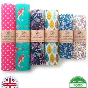 May include: A collection of colorful, reusable beeswax food wraps. Designs include pink polka dots, koi fish, floral patterns, and leaf motifs. Each wrap is labeled with "Honey Bee Good" and "Certified Food Safe". The wraps are handmade in the United Kingdom.