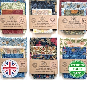 May include: Six sets of three beeswax food wraps featuring various floral and botanical patterns in blue, red, green, and cream. Each set is secured with a brown paper band labeled Honey Bee Good Beeswax Food Wraps, Set of Three, 30cm, 25cm, 20cm.