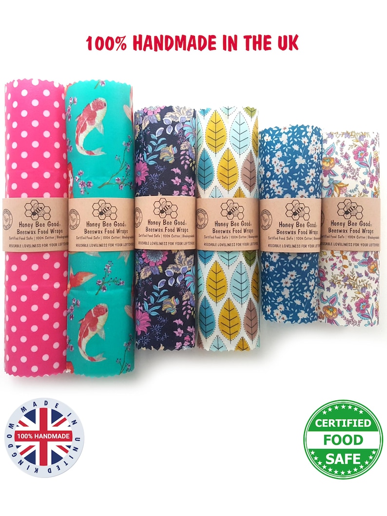 May include: Six rolls of Honey Bee Good Beeswax Food Wraps with various patterns including pink polka dots, koi fish, floral, and leaf designs. Each roll features a brown paper band with the text Honey Bee Good Beeswax Food Wraps.