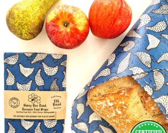 May include: Blue beeswax food wraps featuring a white chicken pattern. The packaging text reads 100% HANDMADE IN THE UK, Honey Bee Good Beeswax Food Wraps, XXL Bread 50x45cm, and CERTIFIED FOOD SAFE. A pear and two apples are visible.