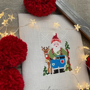 Può includere: Schema di punto croce di Babbo Natale con una renna, circondato da fiocchi di neve. Lo schema è su un tessuto di lino bianco con il testo "myfsnny" nell'angolo in basso a destra.
